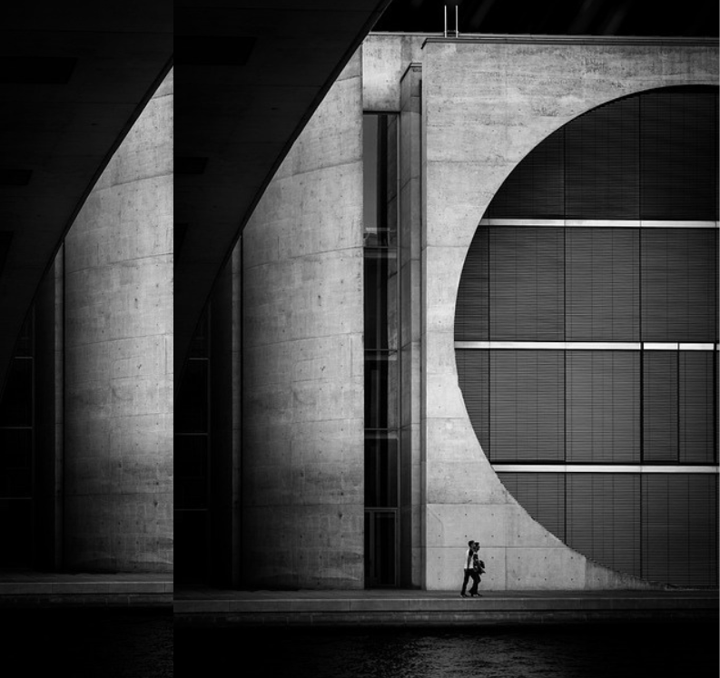 black and white image of a man walking alone in the streets in front of an arts building